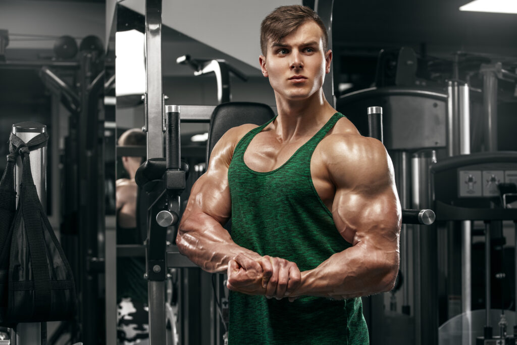 Izmos férfi mutatja az izmait az edzőteremben, férfi nagy bicepszekkel